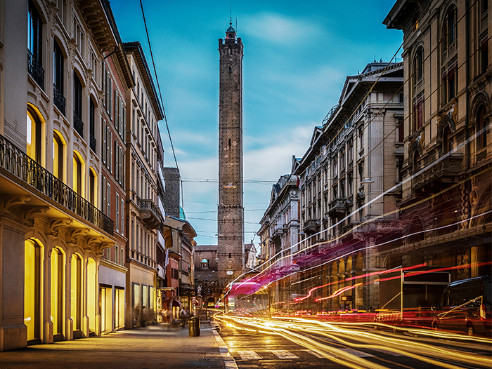 Via Rizzoli Bologna con sullo sfondo la torre degli Asinelli e scie di fanali foto all'imbrunire